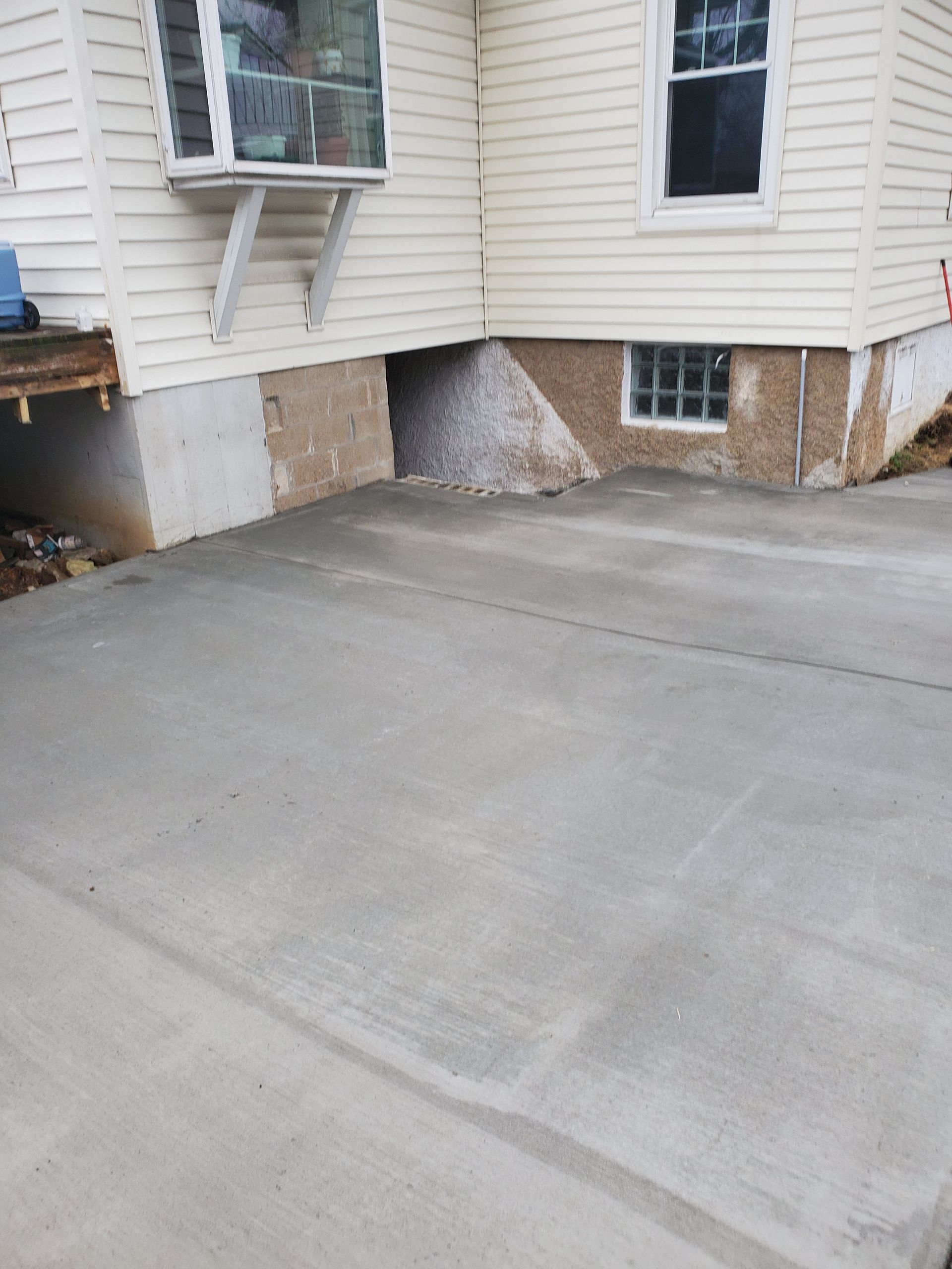 Newly poured concrete patio next to a house with white siding and a small window.