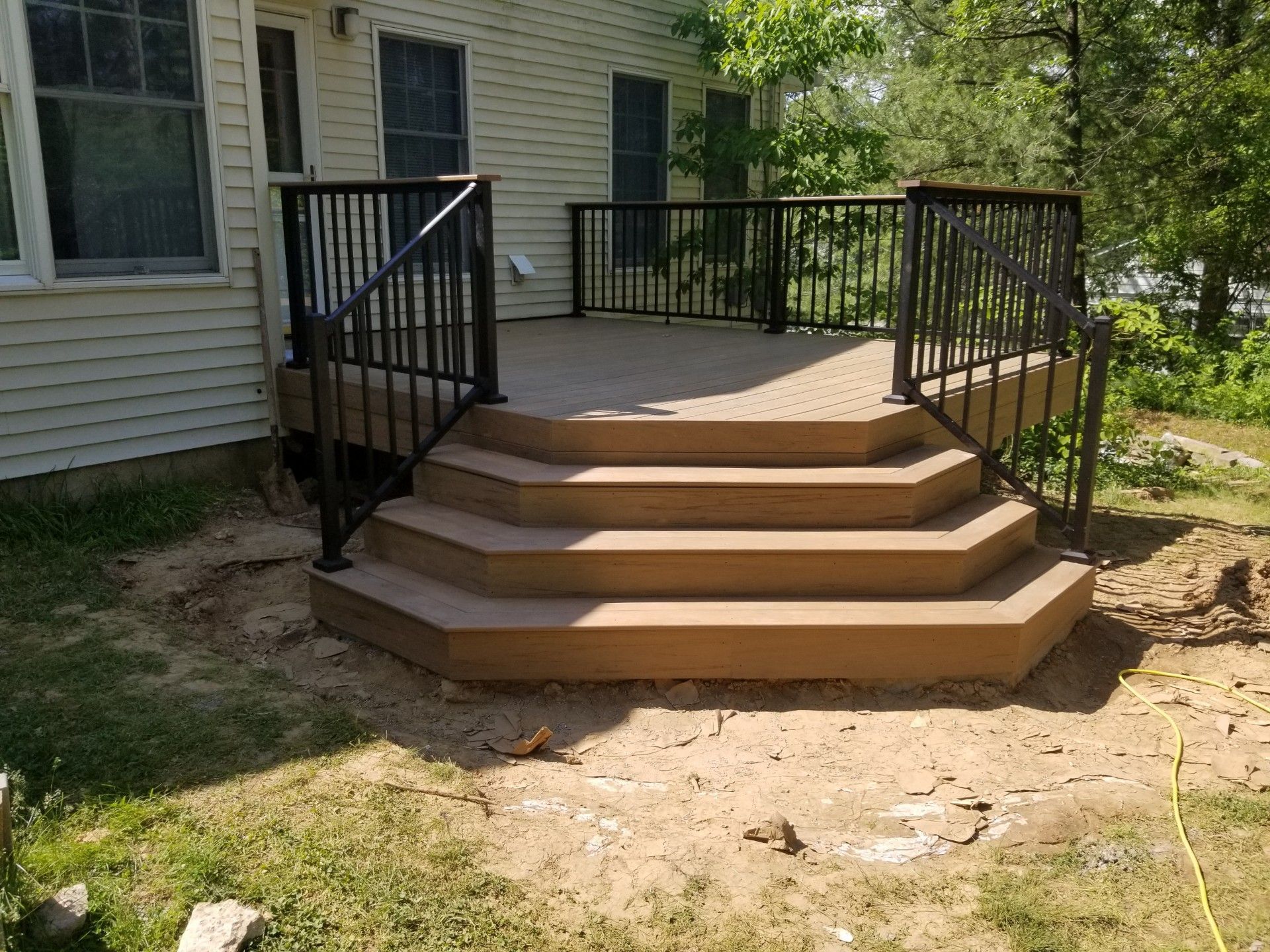 Brown deck with black railing and steps leading to a house, set in a yard.