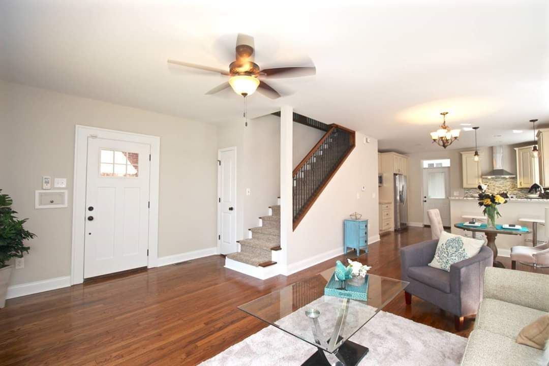 Living room with hardwood floors, stairs, and open kitchen. Beige walls and a gray couch.