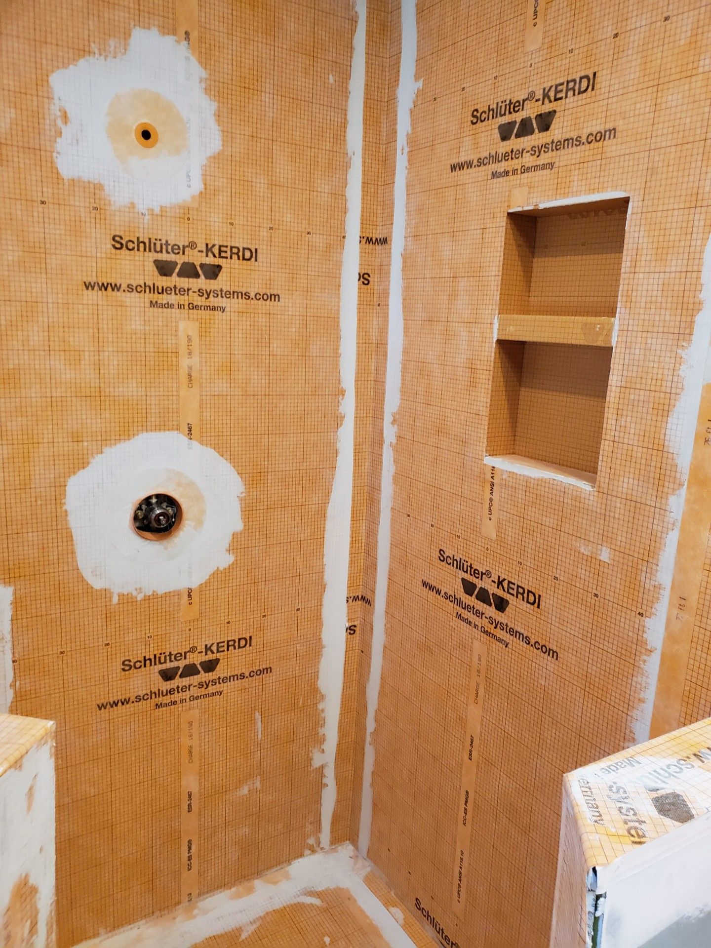 Orange waterproof membrane installed in a shower; white sealant at seams and fixtures.