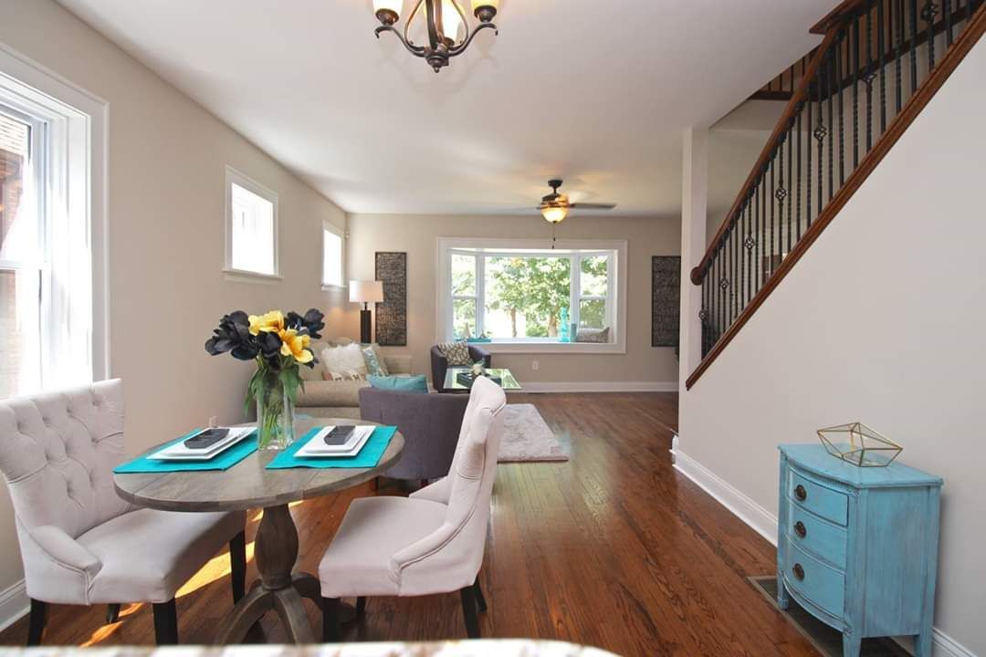 Dining area with round table, upholstered chairs, and wood flooring, leading to living room and stairs.