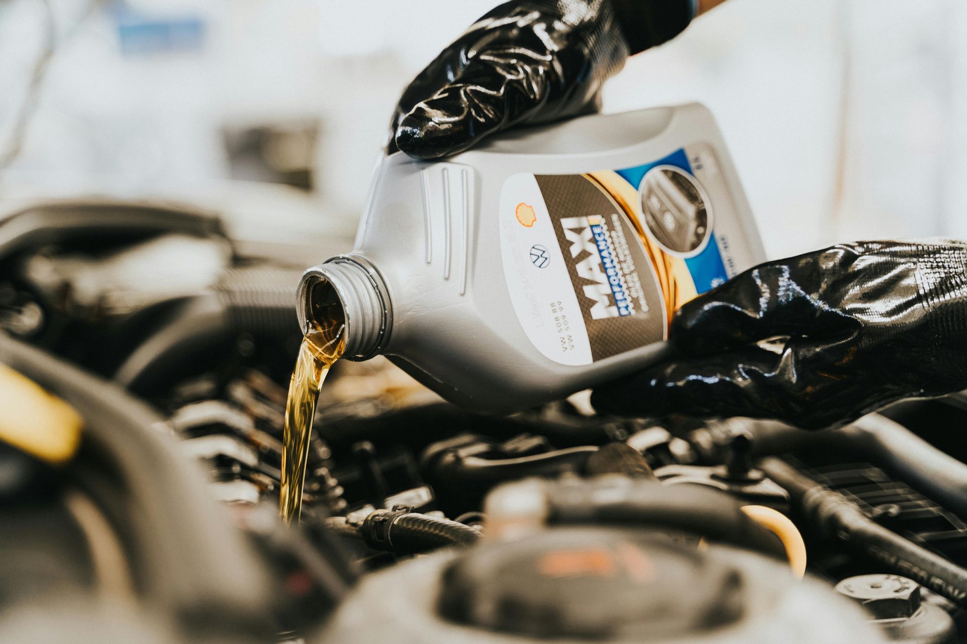 A person in black gloves pours golden motor oil into a car engine.