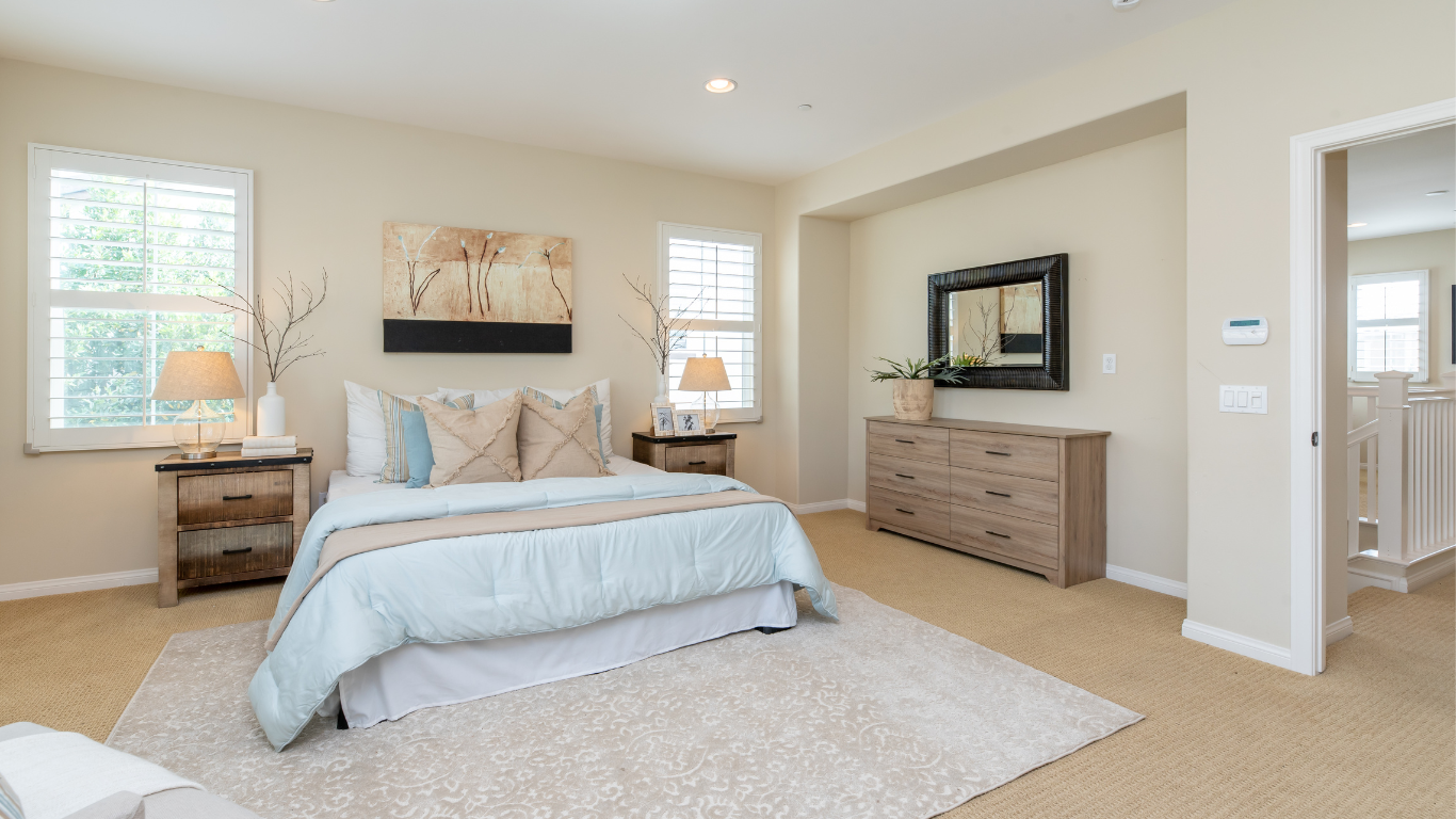 Bedroom with light blue bedding, tan walls, neutral furniture, and rug.