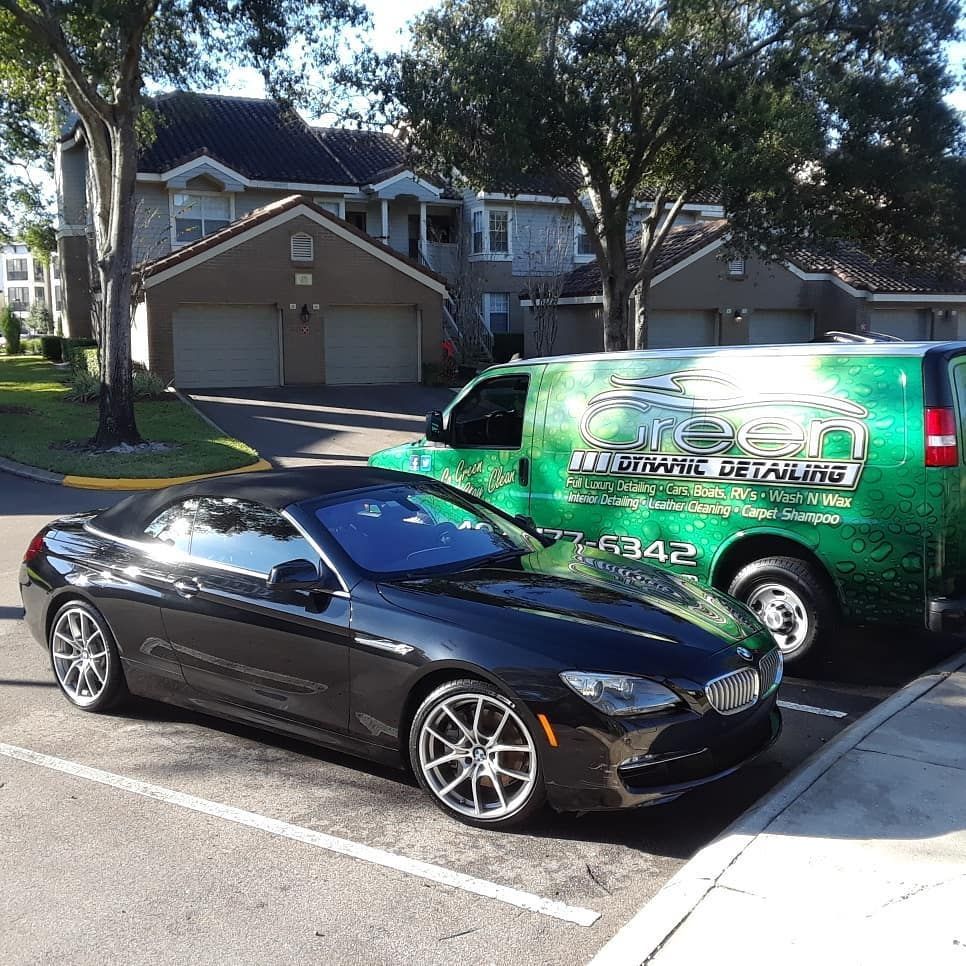 A black convertible car is parked in a parking lot next to a green van.