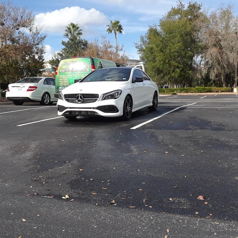 A white car is parked in a parking lot next to a green van