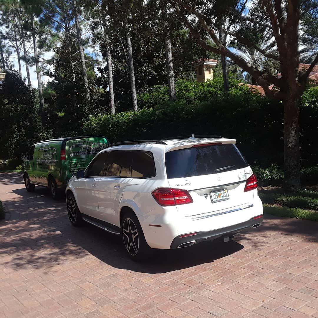 A white suv is parked on a brick driveway next to a green van.