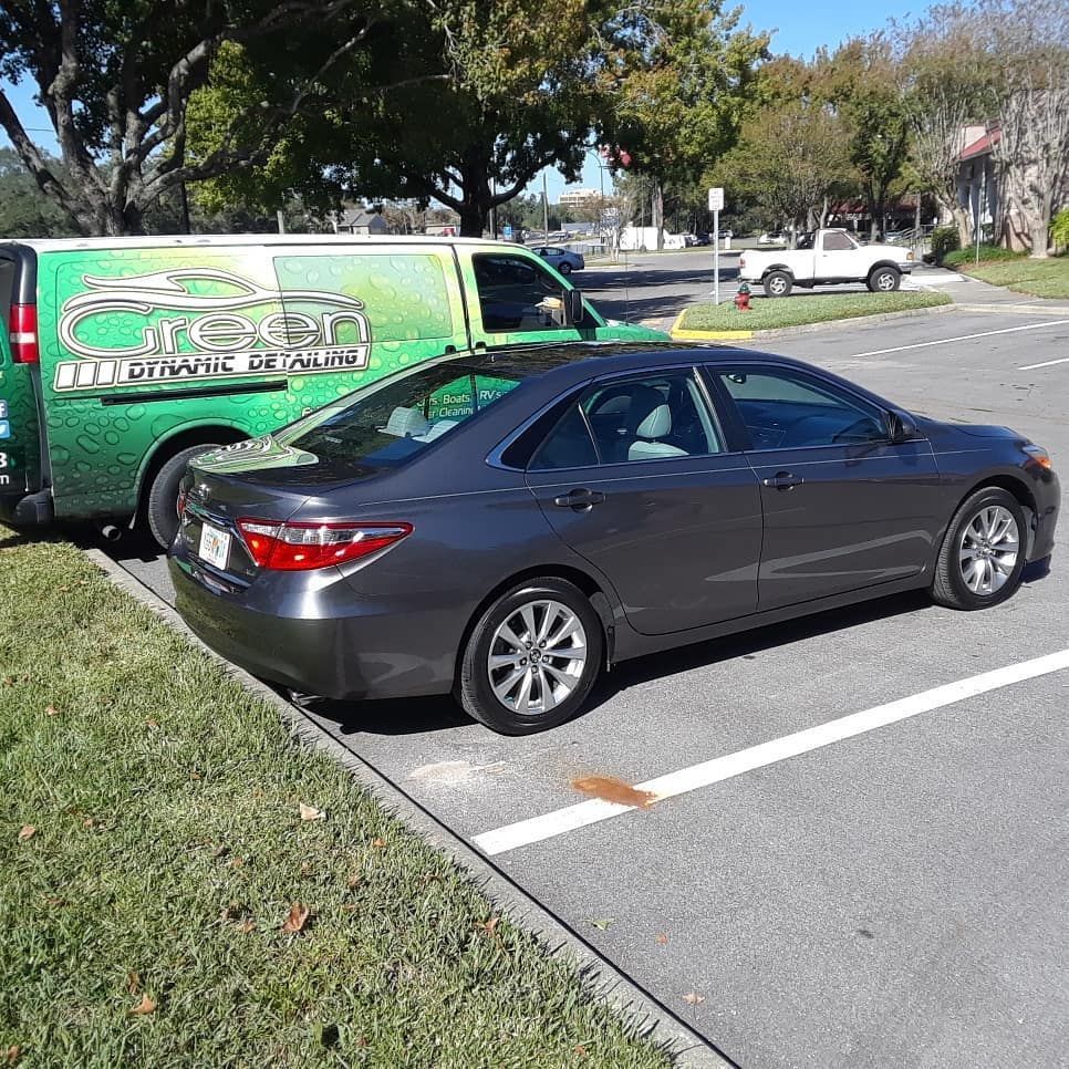 A gray car is parked in a parking lot next to a green van.