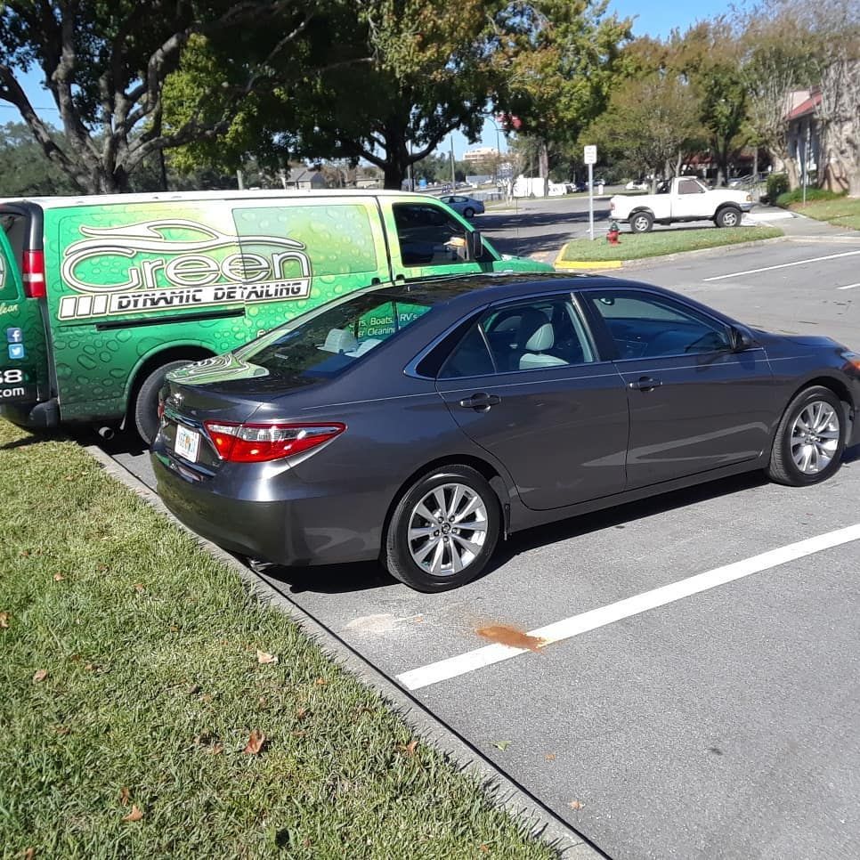 A green van is parked next to a black car