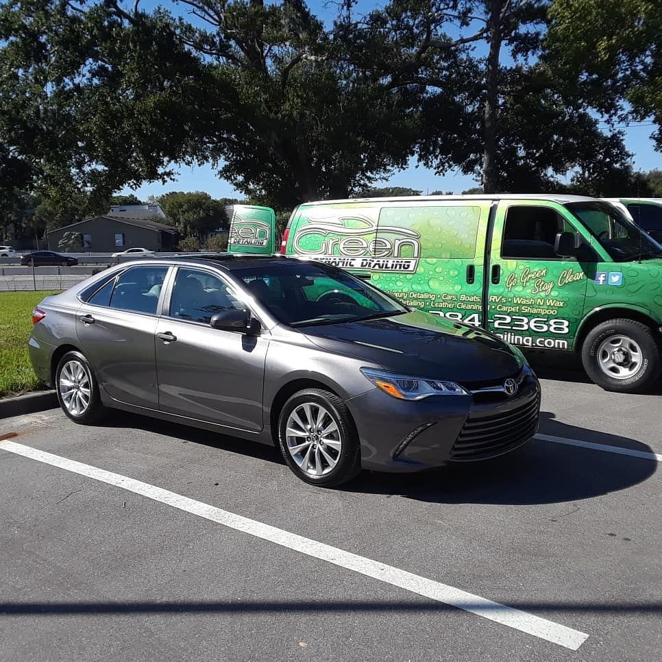 A gray car is parked in a parking lot next to a green van.