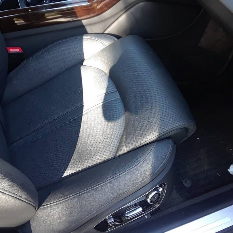 A black leather car seat with a red seat belt buckle