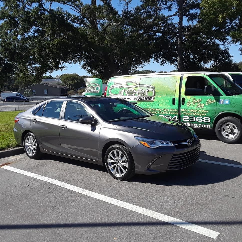 A gray car is parked in a parking lot next to a green van.
