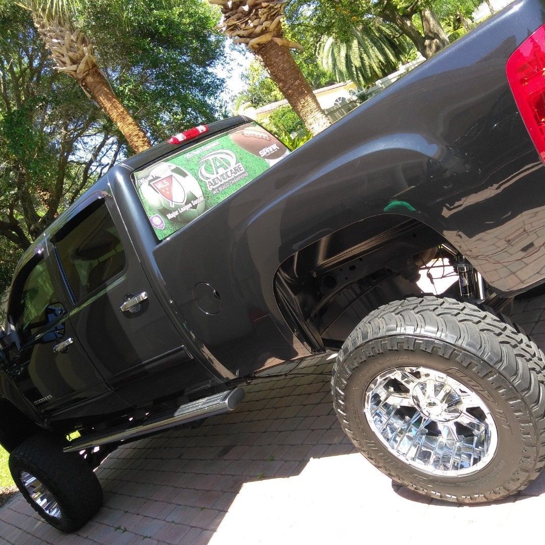 A black truck is parked in a driveway with trees in the background