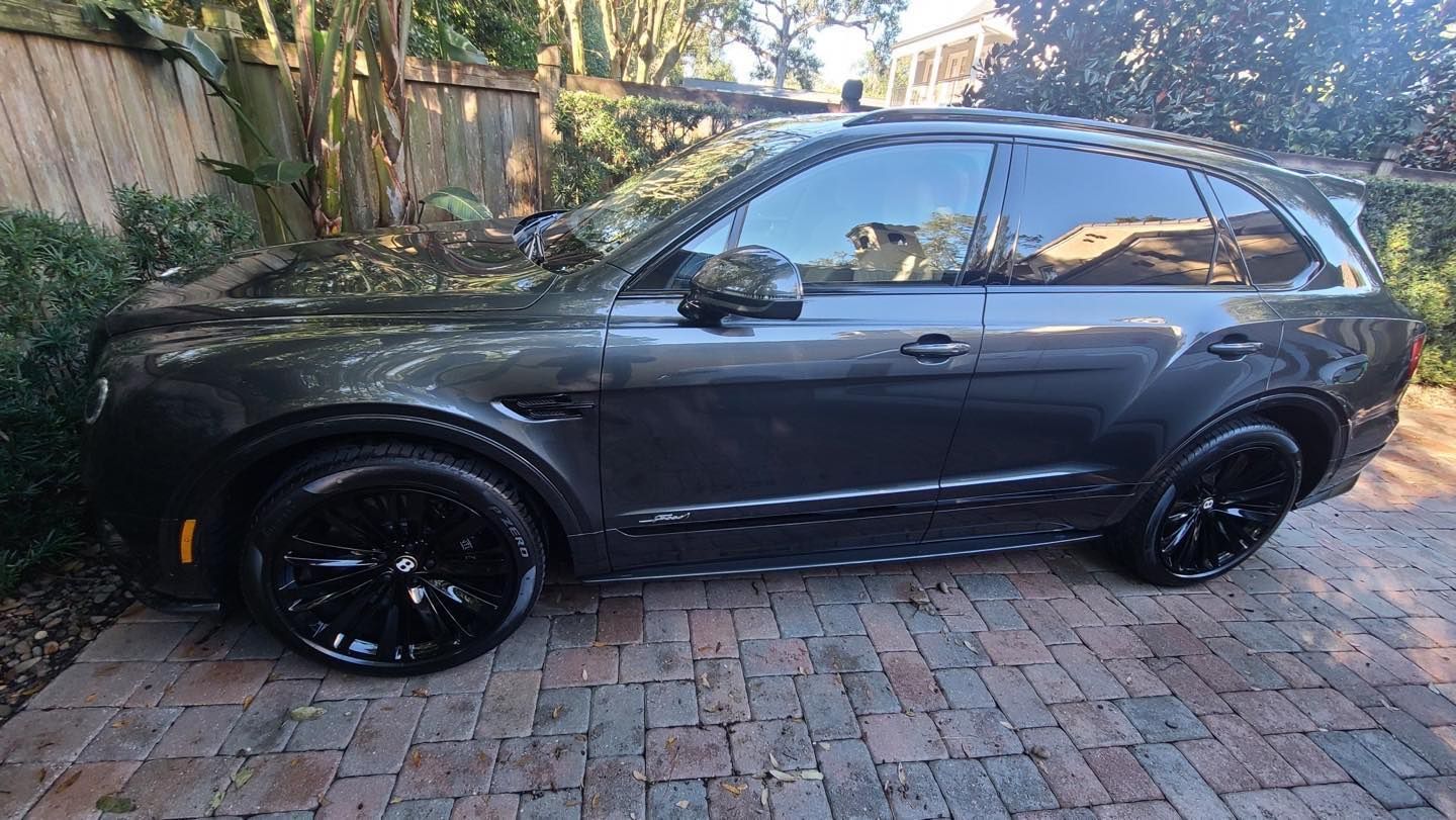 A black bentley bentayga is parked on a brick driveway.