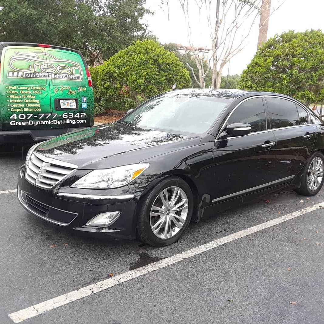 A black car is parked in a parking lot next to a green van.