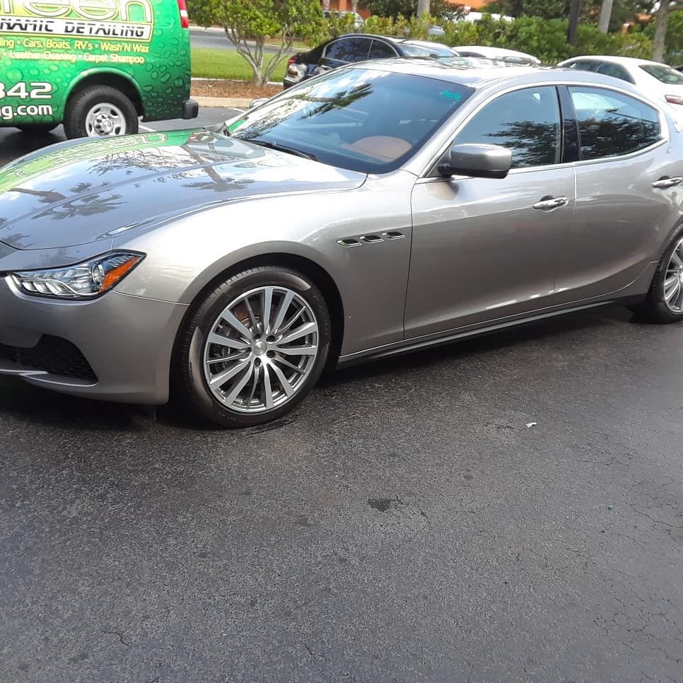 A silver car is parked next to a green van that says universal detailing