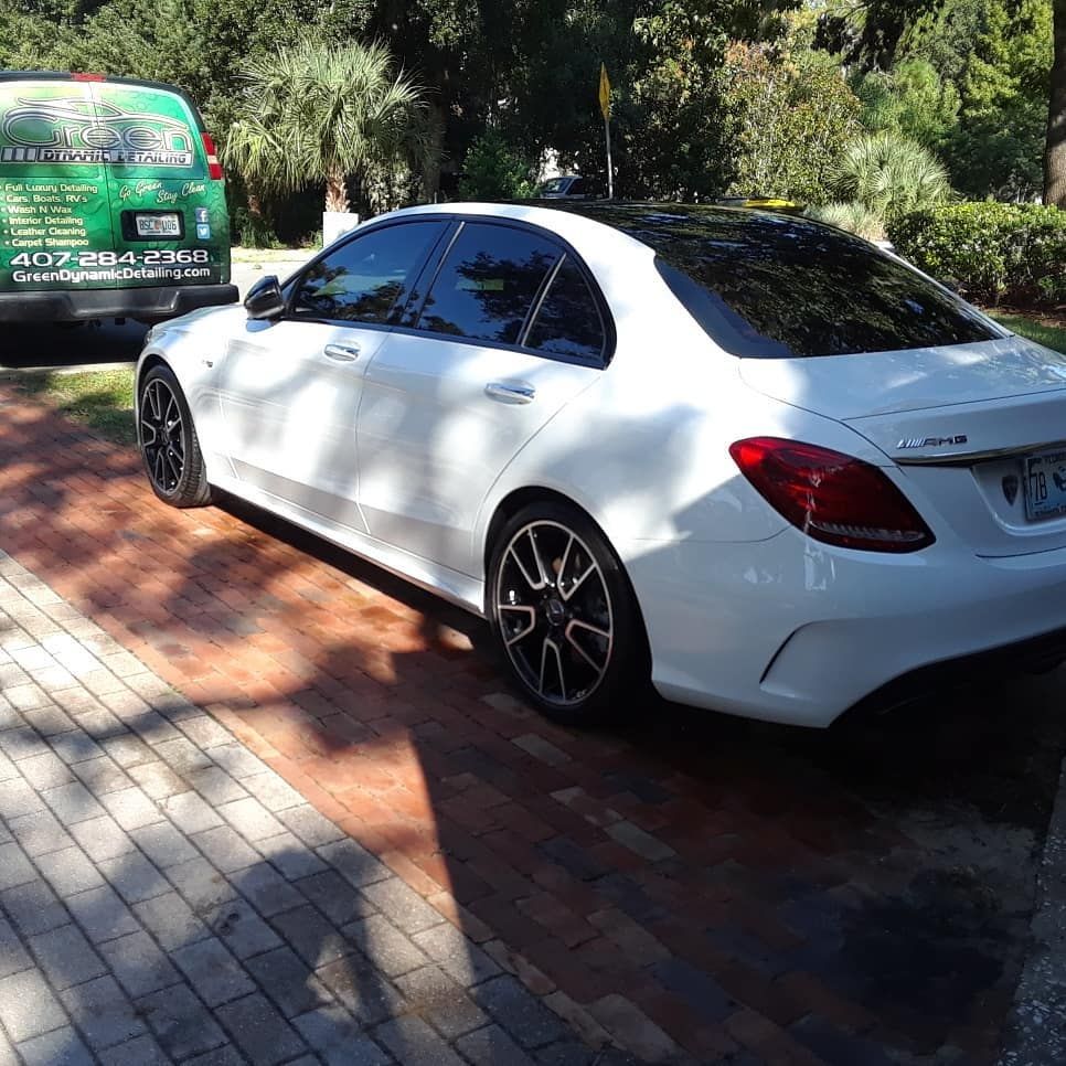 A white car is parked on a brick driveway next to a green van