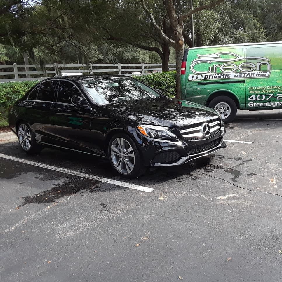 A black mercedes benz is parked in a parking lot next to a green van.