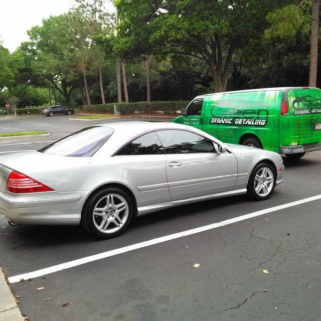 A silver car is parked next to a green van that says www.detailing