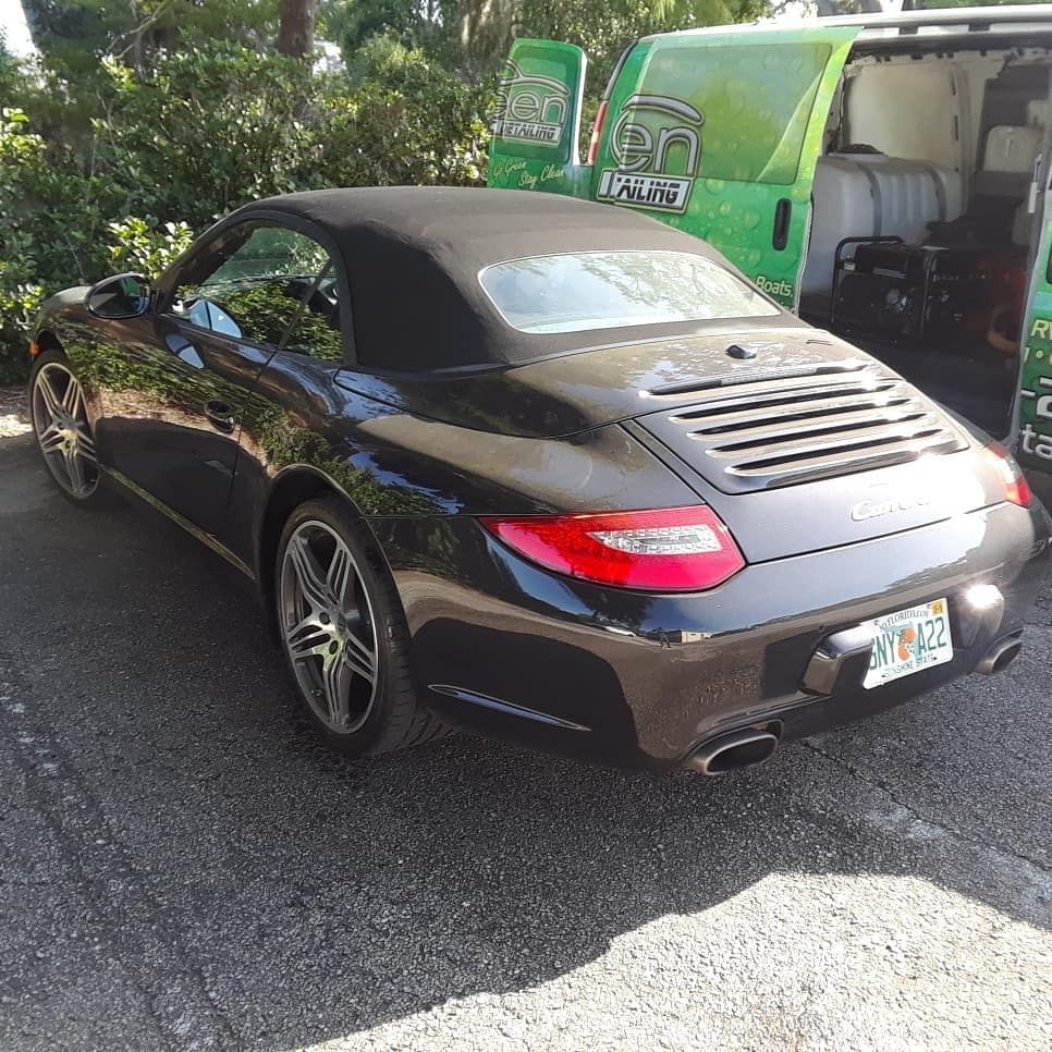 A black porsche convertible is parked next to a green van