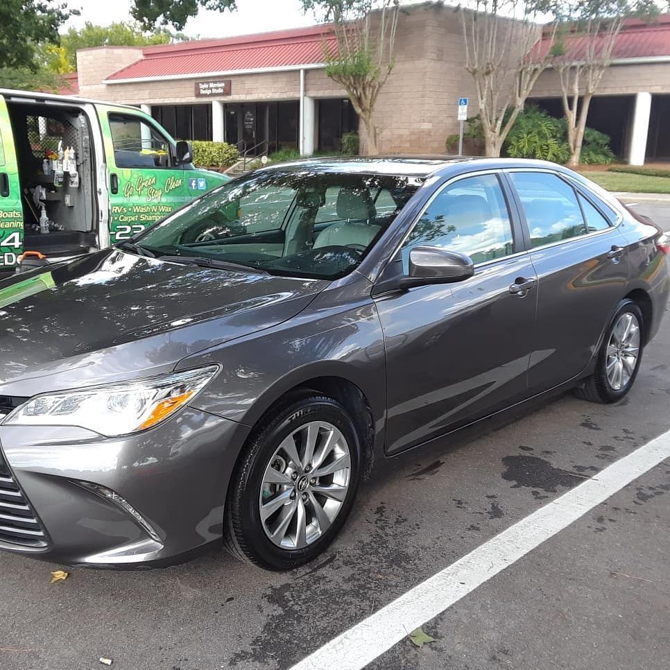 A gray car is parked in a parking lot next to a green van.