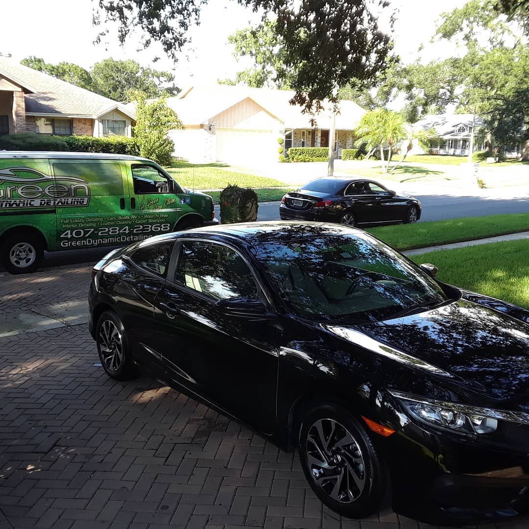 A black car is parked on a brick driveway next to a green van.