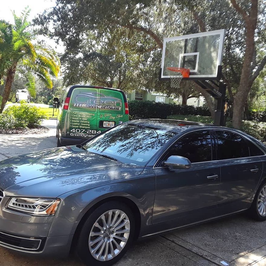 A gray car is parked in a driveway next to a basketball hoop.