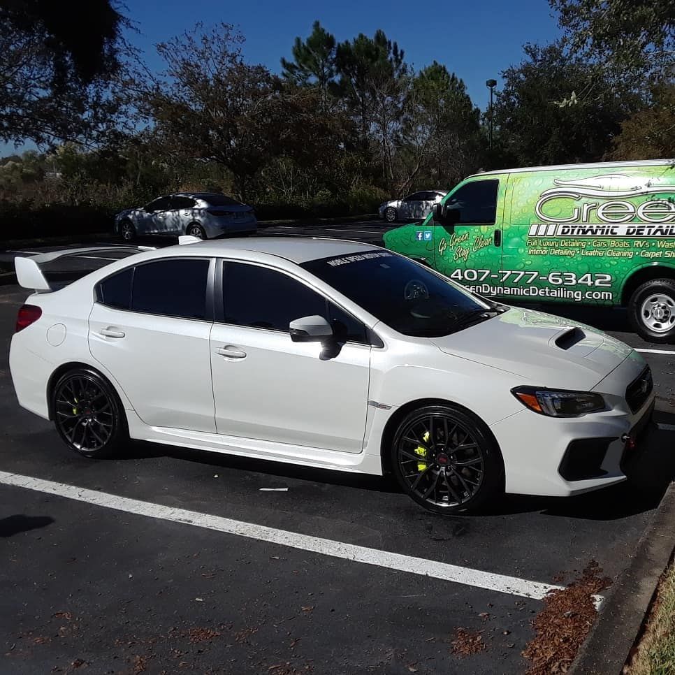 A white car is parked in a parking lot next to a green van.