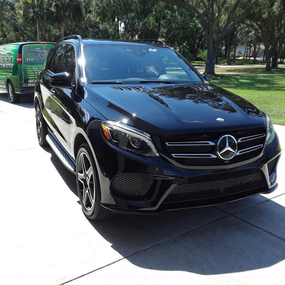 A black mercedes is parked in a driveway next to a green van