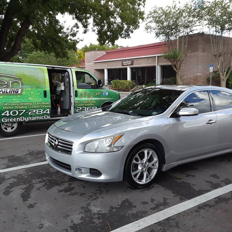 A silver car is parked in a parking lot next to a green van.