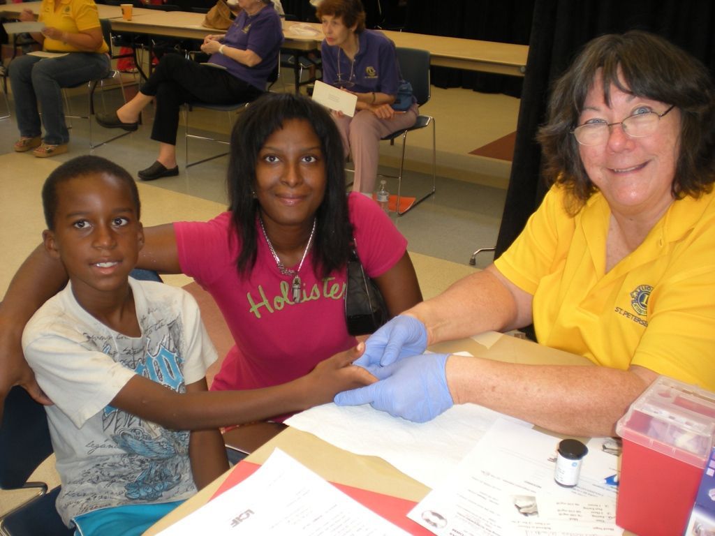 3 people sitting at a table. 1 wearing gloves holding the hand of another