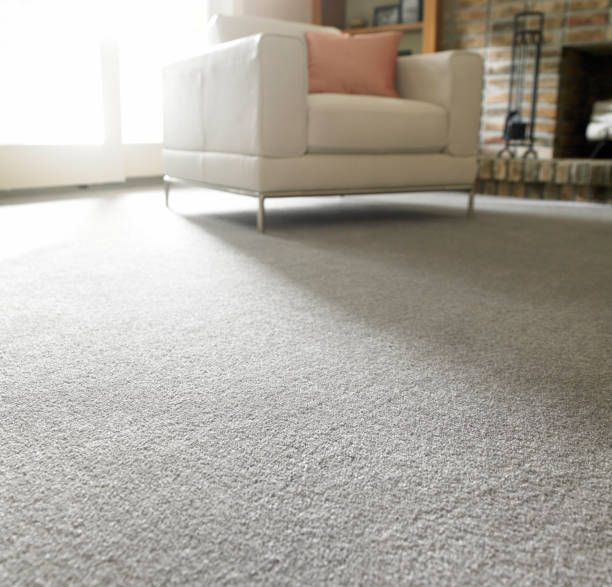 A low-angle view of a grey carpet in a living room with a white armchair and a peach pillow near a stone fireplace.