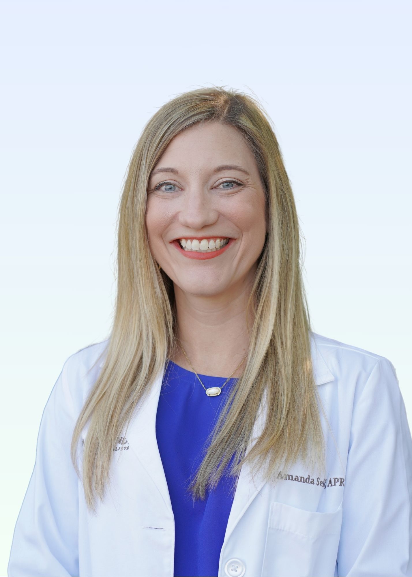 A woman in a white lab coat and blue shirt is smiling for the camera.