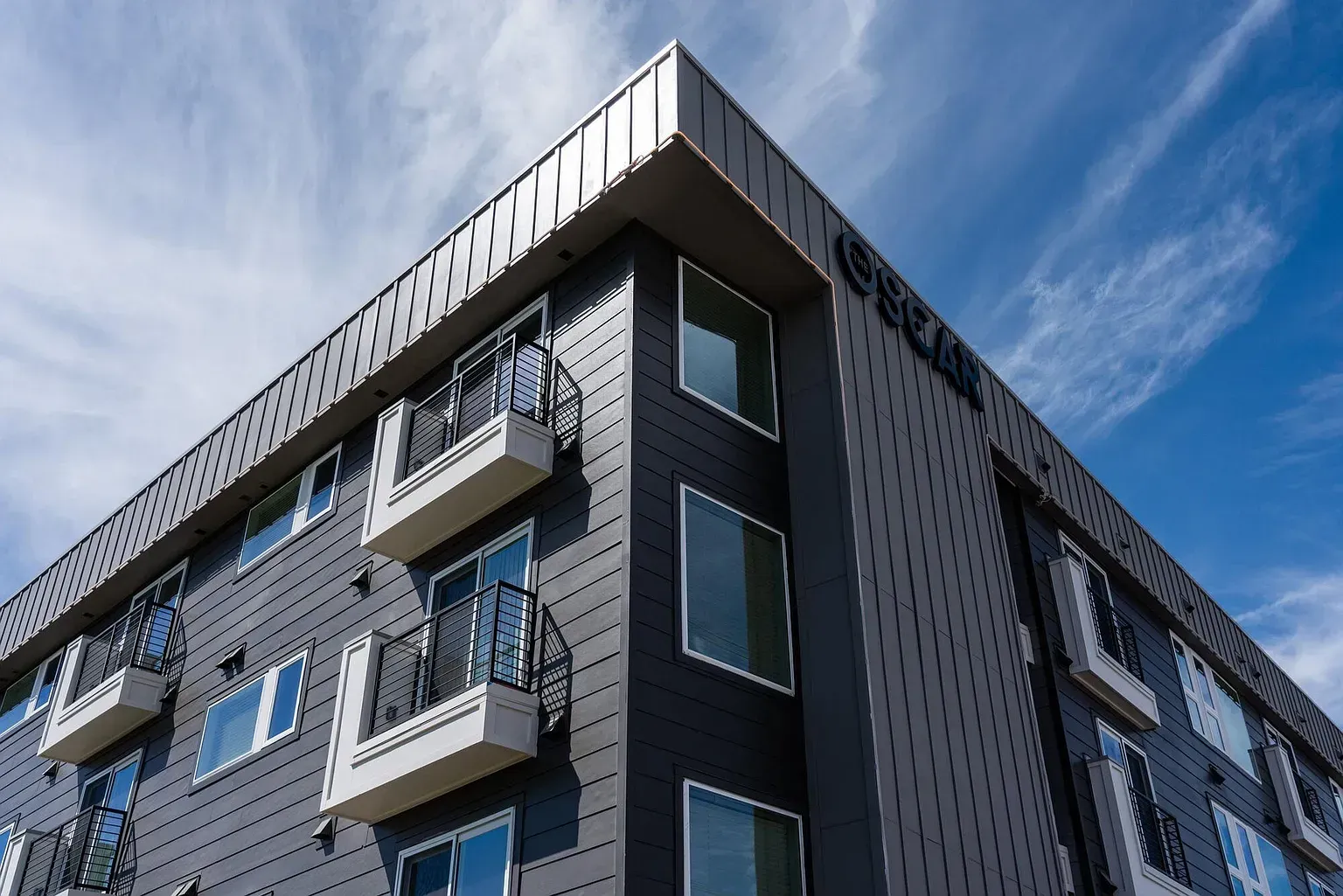 Exterior view of a modern gray apartment building with multiple balconies under a blue sky.