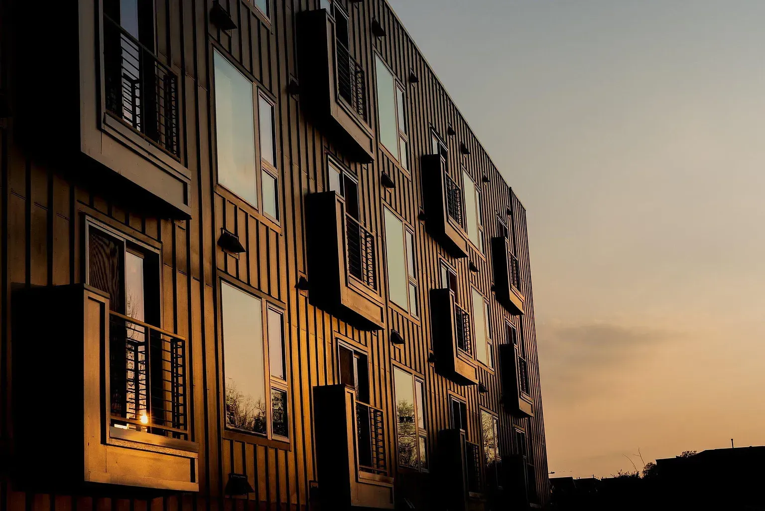 Sunset view of a modern apartment building facade with multiple balconies.