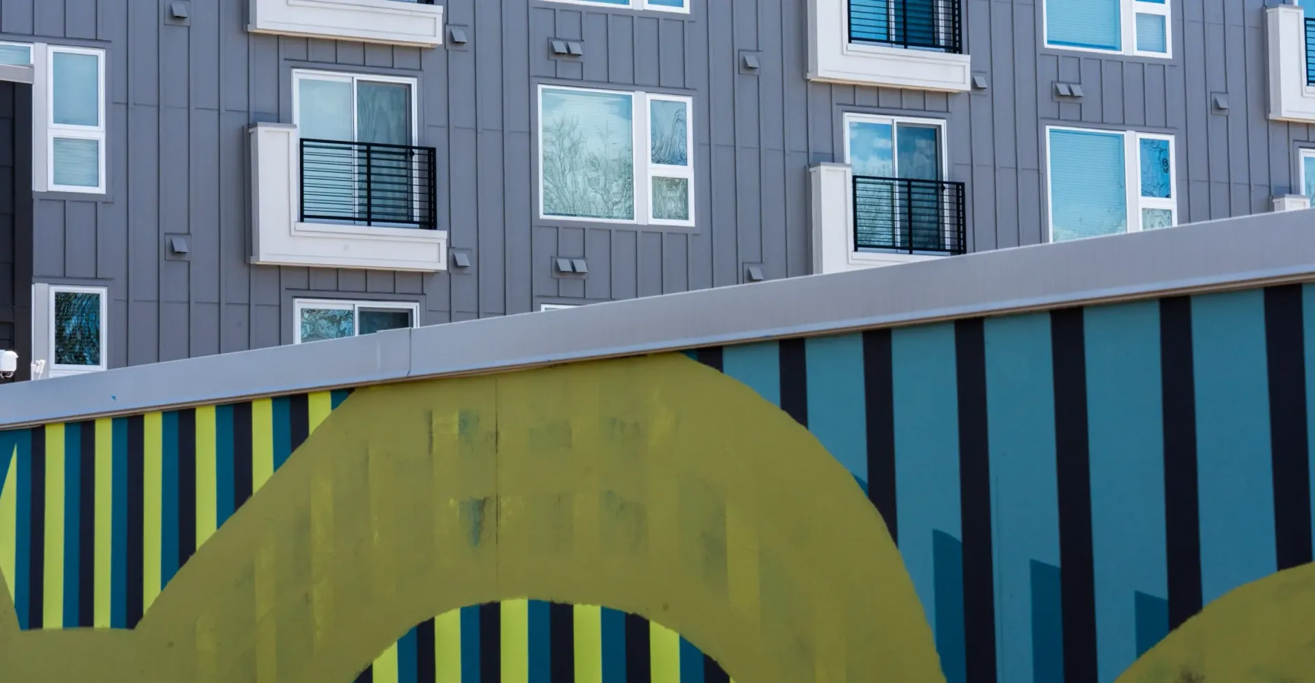 Exterior view of a modern apartment building with small balconies and a colorful mural in the foreground.
