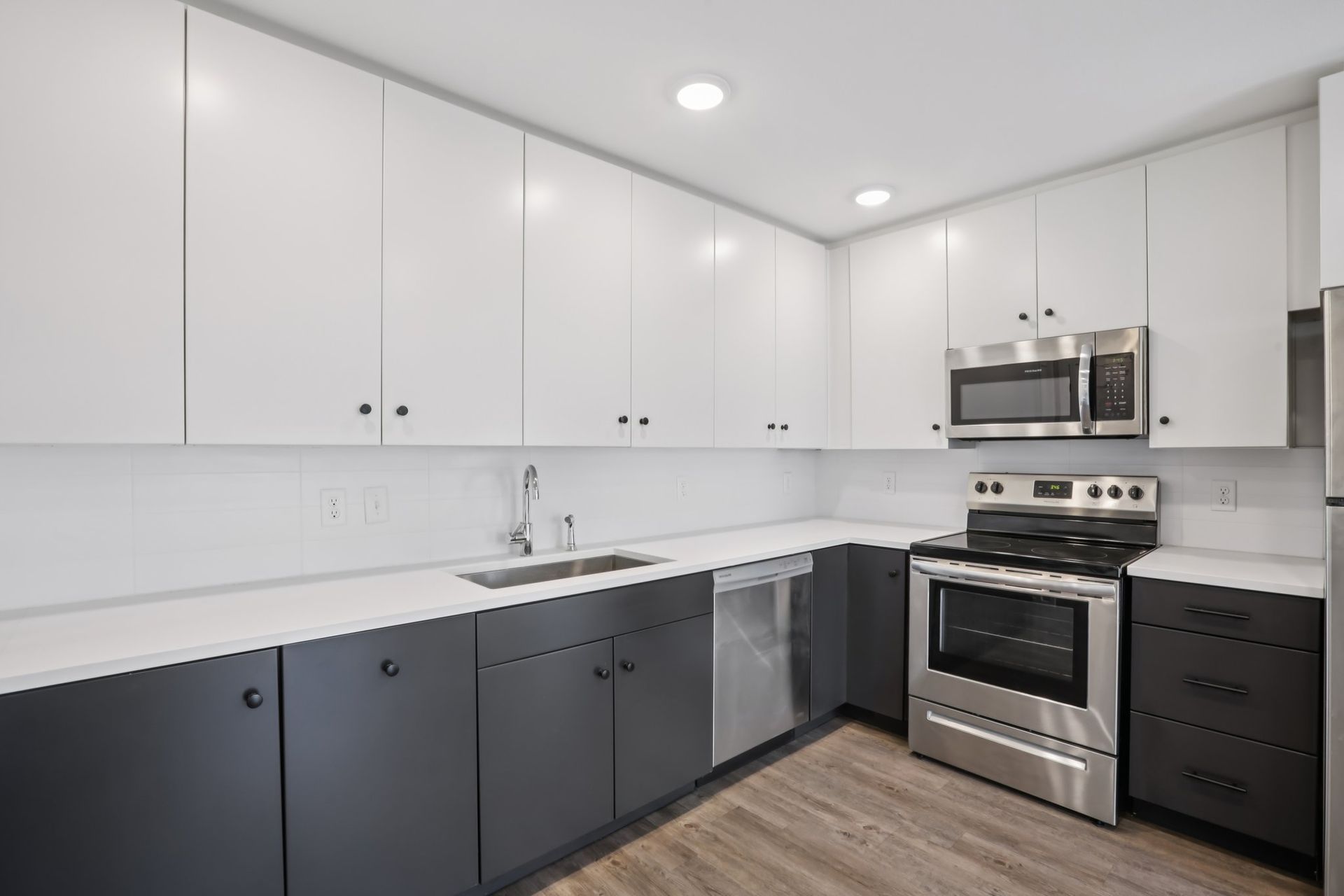 Modern kitchen with two-tone cabinetry featuring white upper cabinets and dark gray lower cabinets on wood-look flooring.