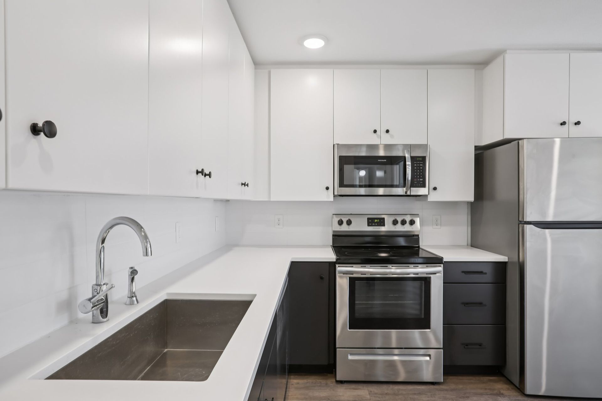 Modern kitchen with white upper cabinets, dark lower cabinets, white countertops, and stainless steel appliances.