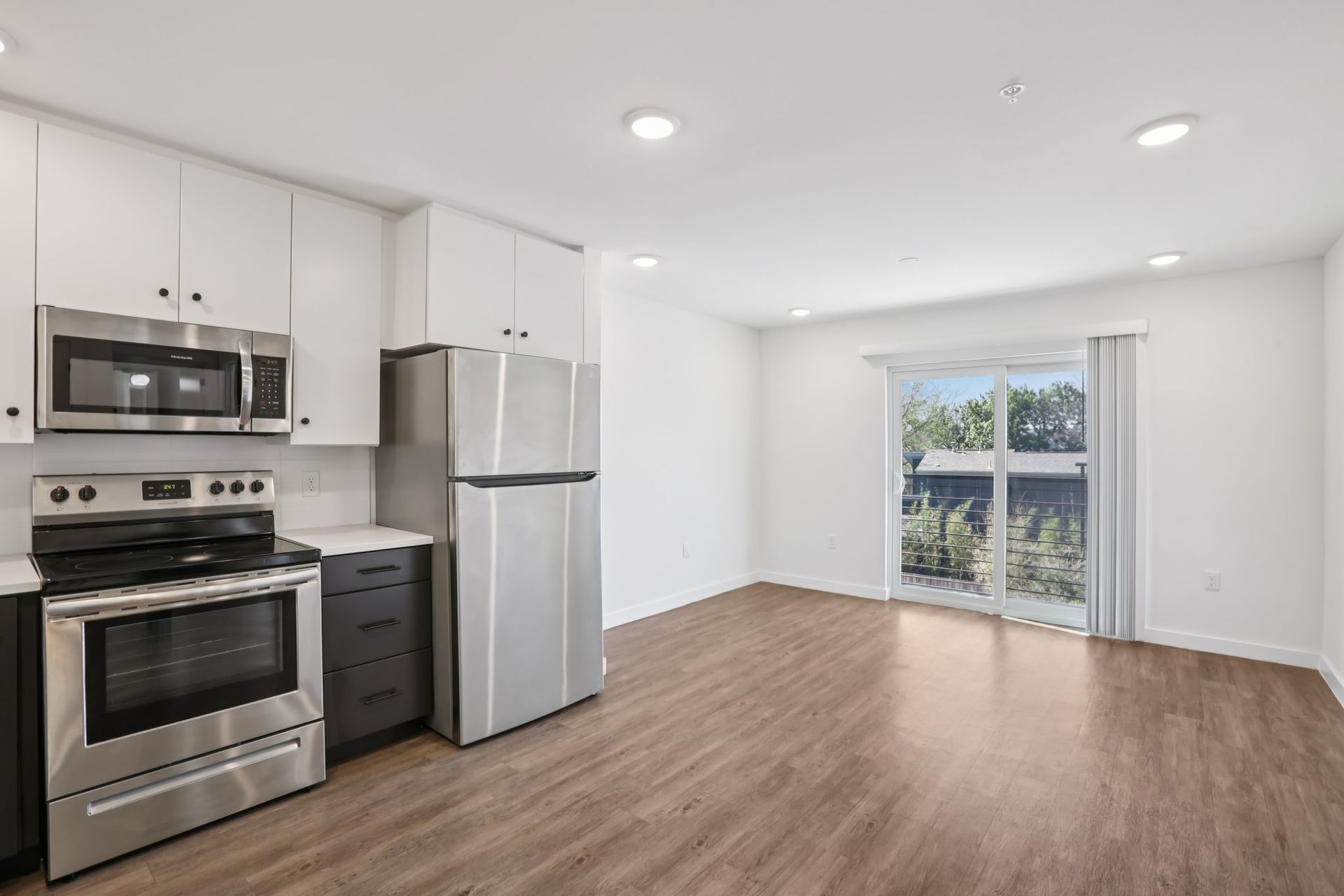 A modern kitchen featuring white cabinets, stainless steel appliances, dark grey drawers, and light wood-look flooring.