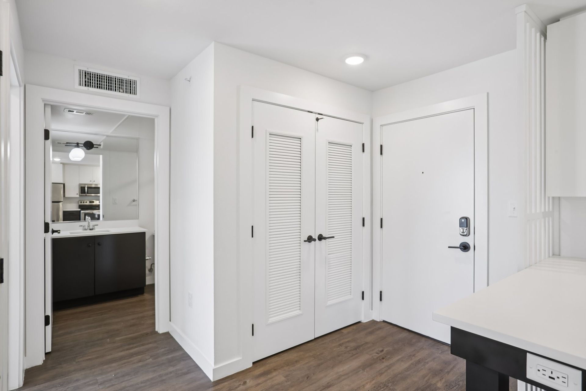 A bright, modern entryway with white walls, wood floors, a closet with patterned glass doors, and a bathroom doorway.