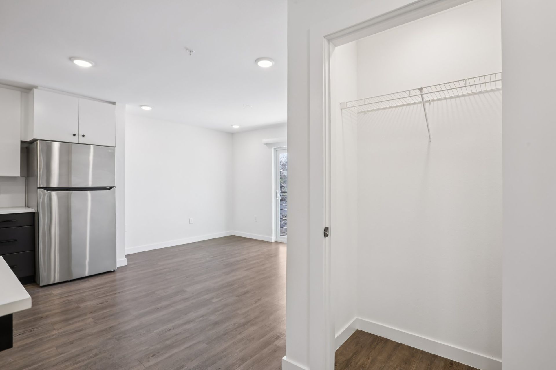 A bright, modern kitchen with a stainless steel refrigerator and an adjacent closet with a hanging rack on white walls.