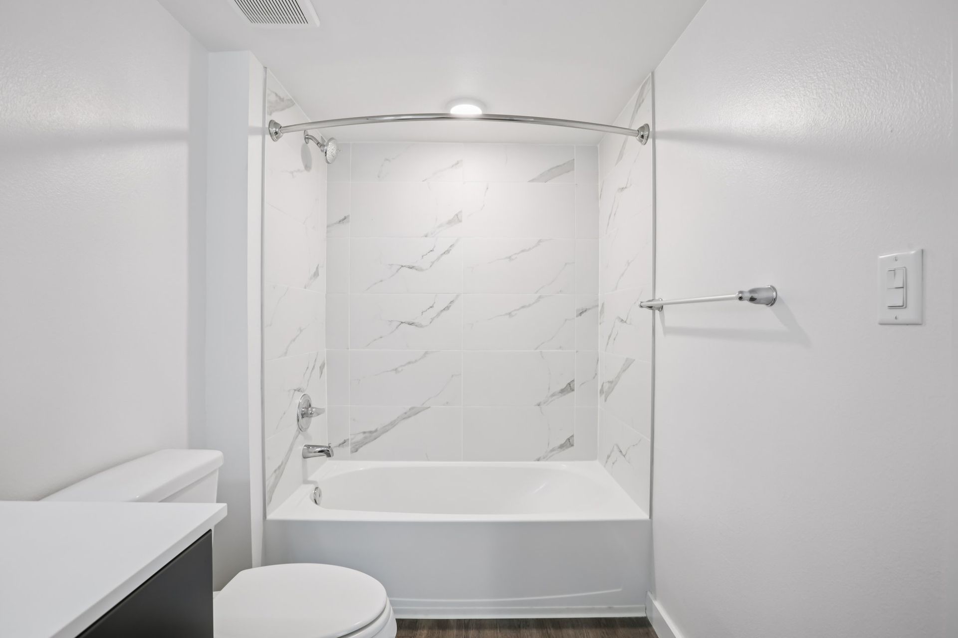 A small, modern bathroom featuring a white bathtub with marble-patterned wall panels, a toilet, and a vanity.