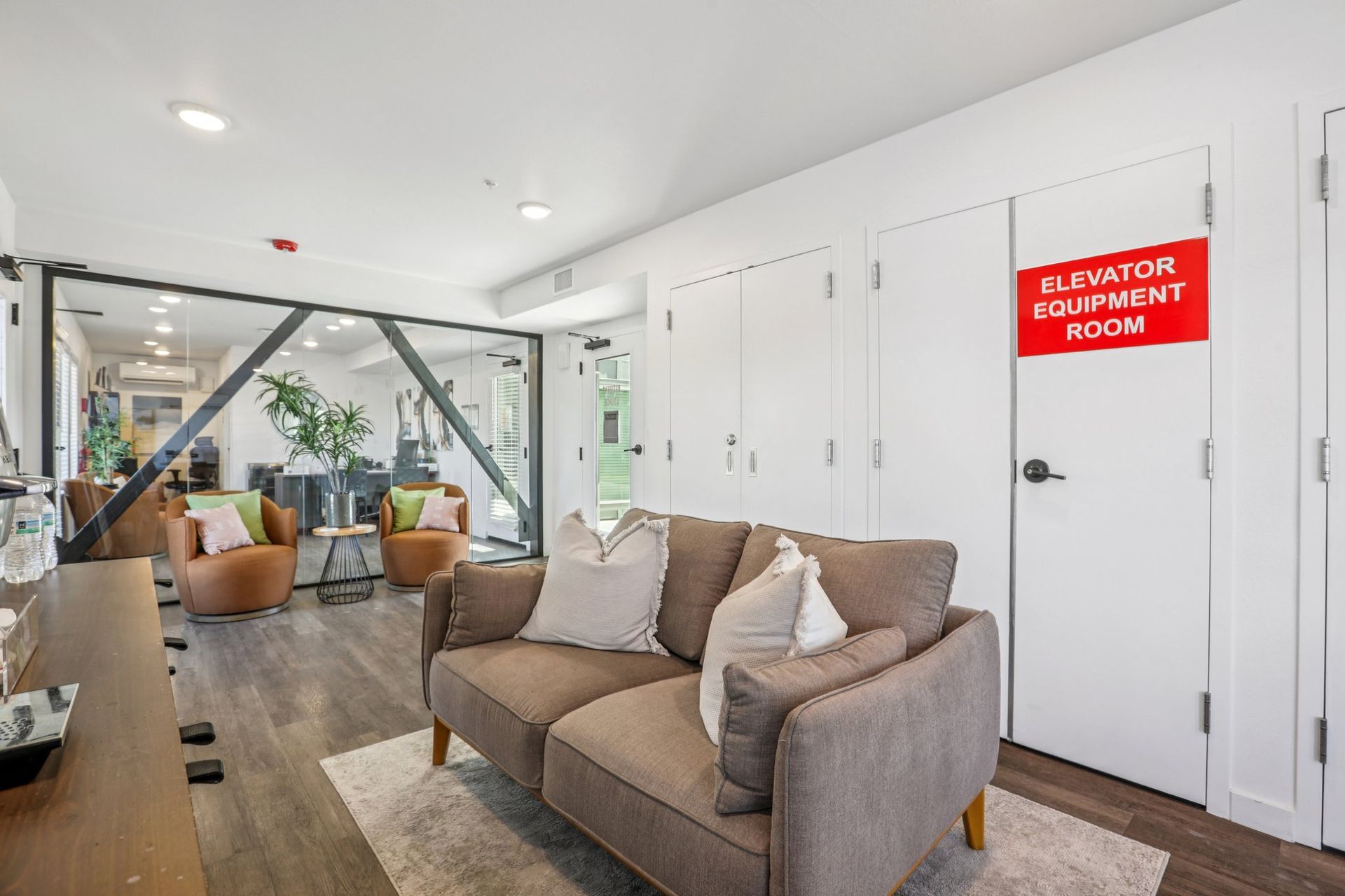 A modern lobby waiting area with a brown loveseat, armchairs, and a door marked 