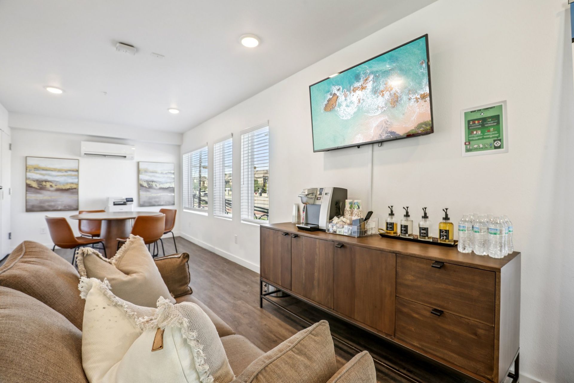 Modern hotel lobby with a sofa in the foreground, a wooden sideboard with coffee service, and a television on the wall.