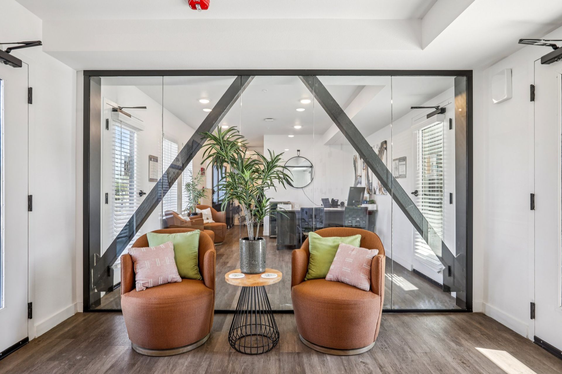 Two brown armchairs with pink and green pillows face each other with a small table and potted plant in front of glass doors.