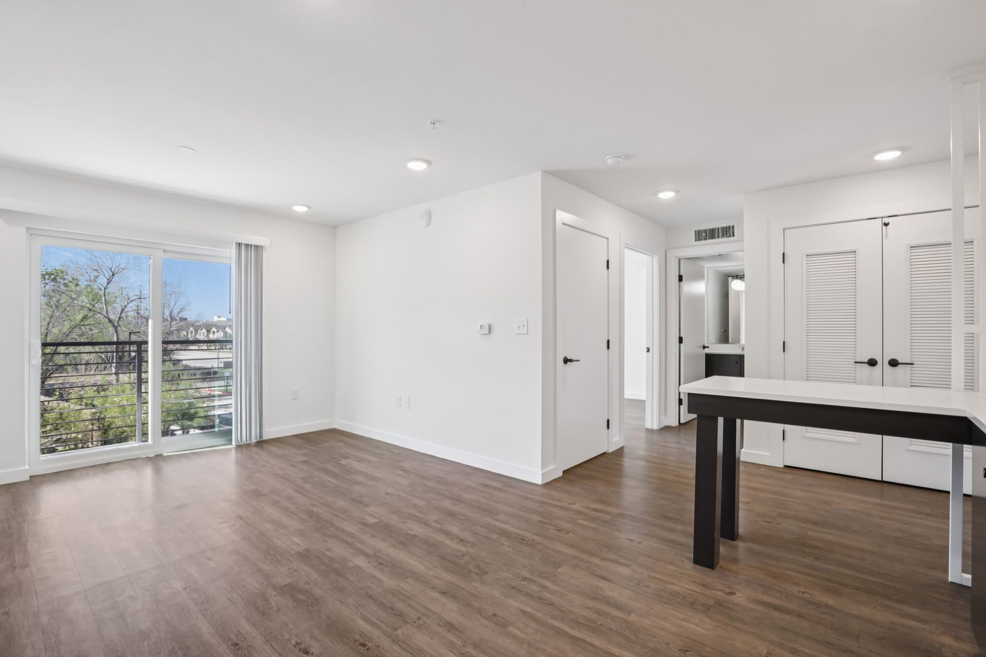 A bright, minimalist room with white walls, wood-look flooring, a glass sliding door, and a white kitchen island.
