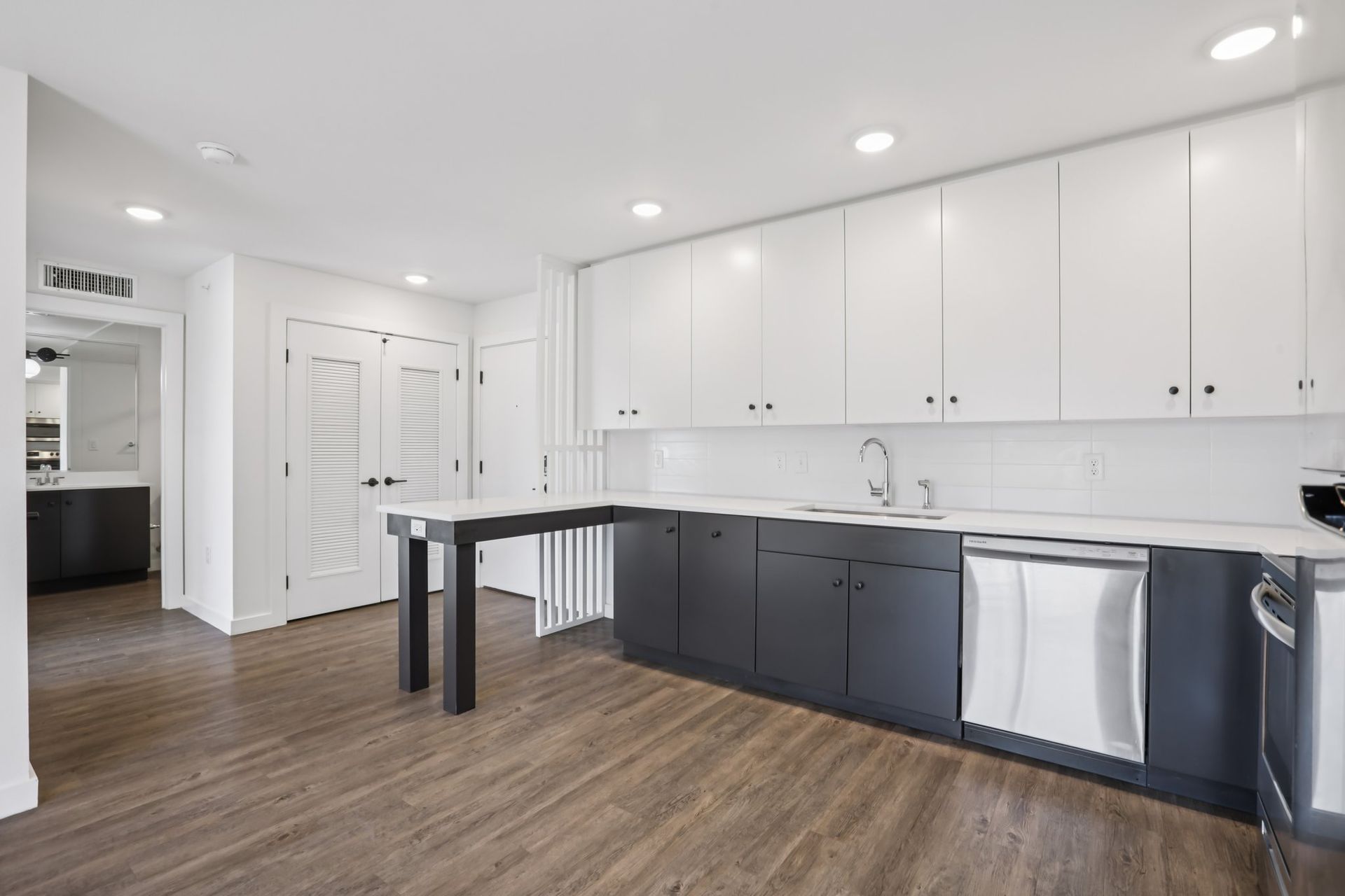 A modern kitchen with white upper cabinets, dark lower cabinets, a wooden floor, and a small peninsula.