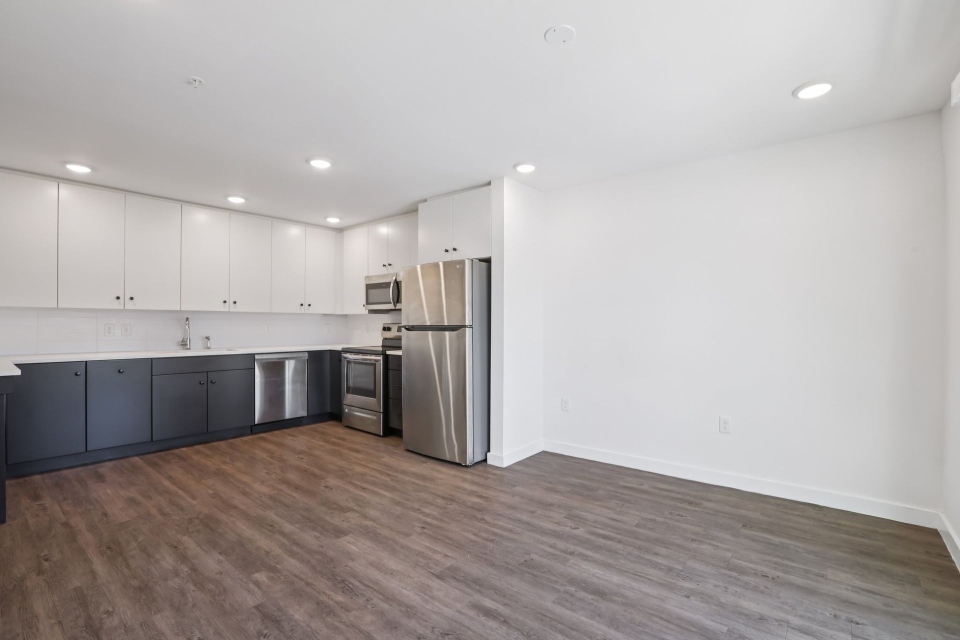 A modern kitchen with two-toned white and dark gray cabinetry, stainless steel appliances, and wood-look flooring.