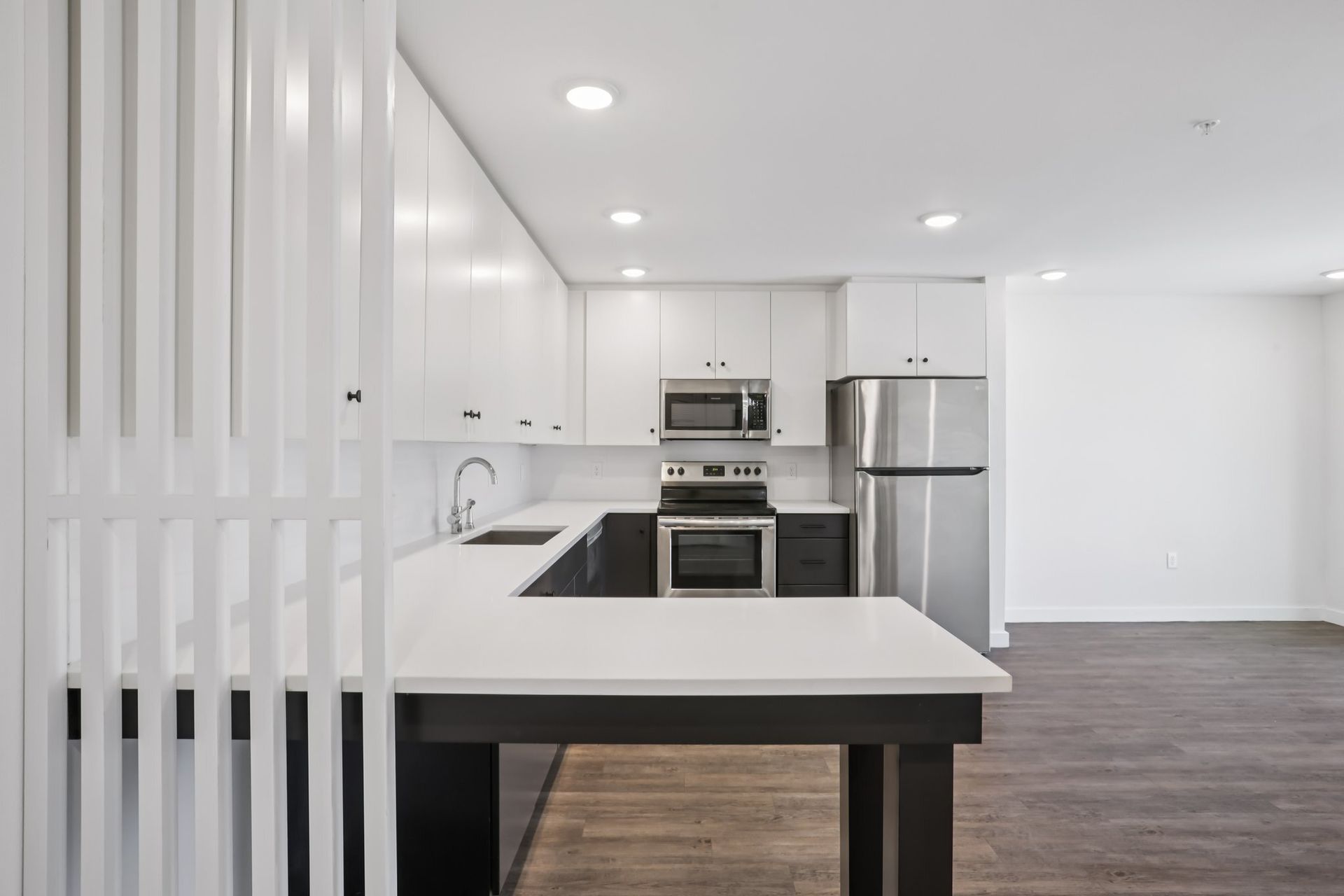 A modern kitchen featuring white upper cabinets, dark base cabinets, white countertops, and stainless steel appliances.