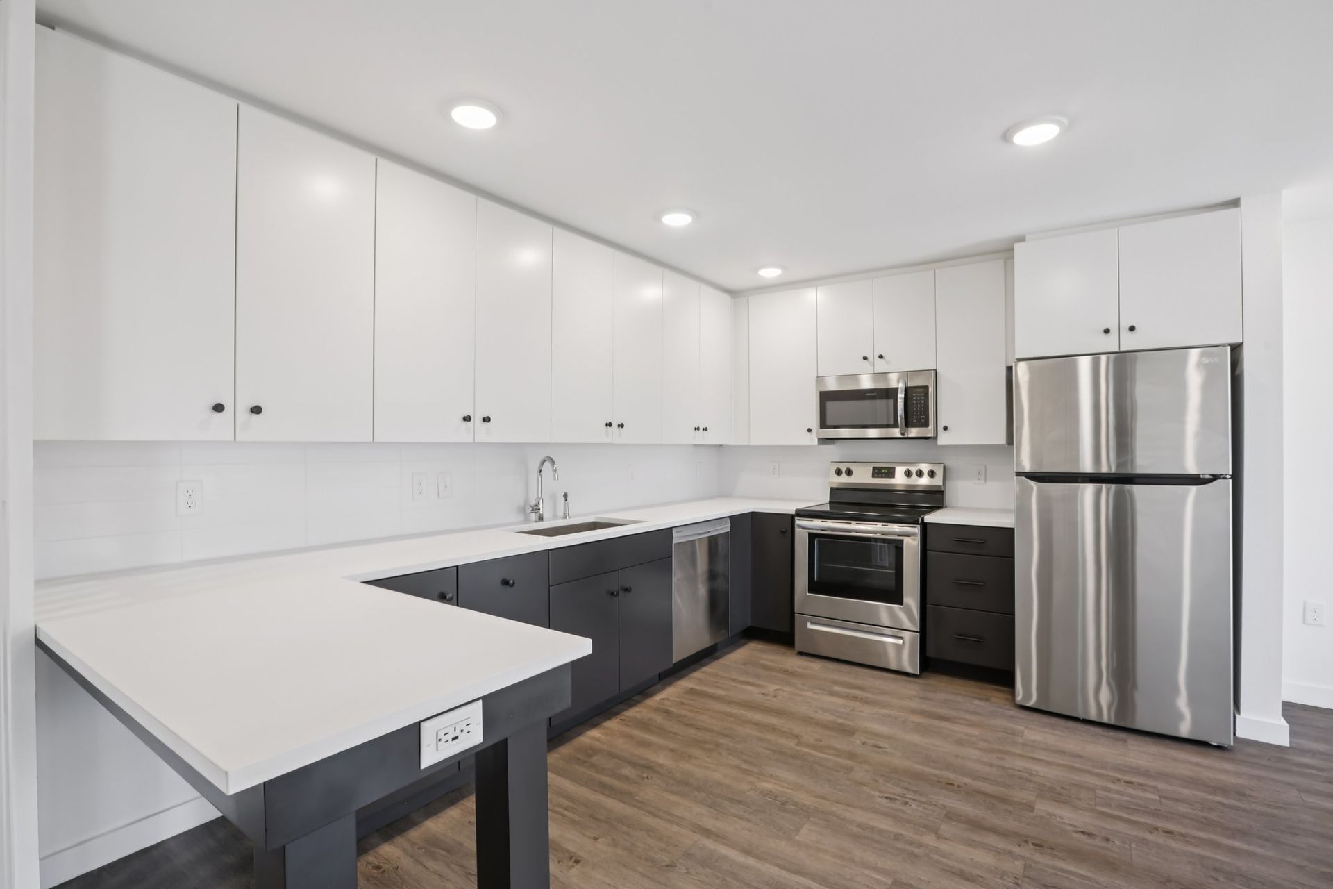 Modern kitchen with white upper cabinets, dark lower cabinets, stainless steel appliances, and a white peninsula counter.
