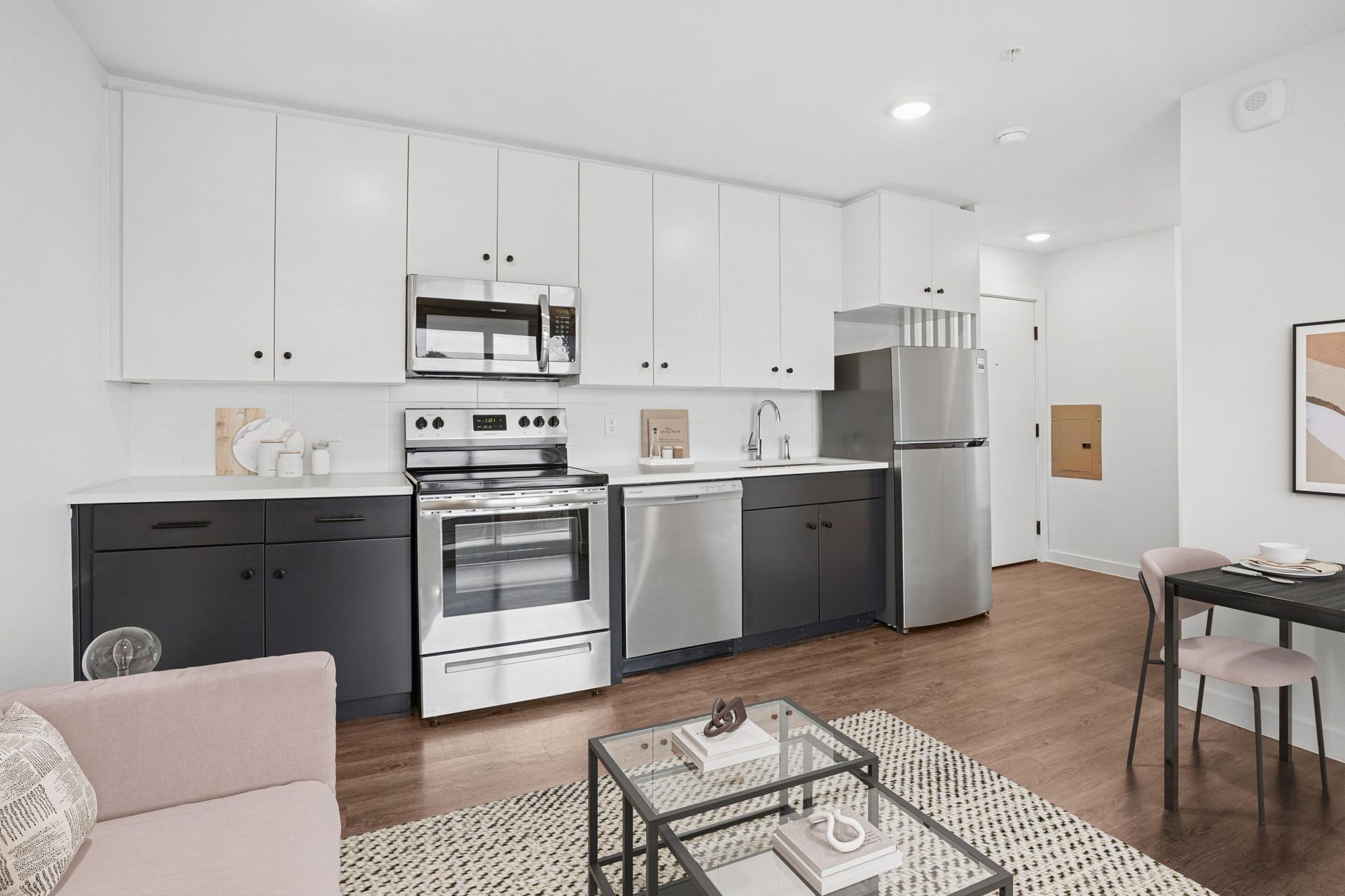 Modern kitchen with white upper cabinets, dark lower cabinets, stainless steel appliances, and wood-style flooring.